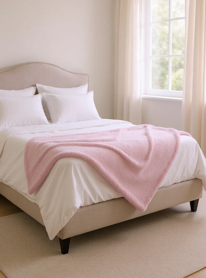 Plaid rose plié au pied du lit — chambre lumineuse